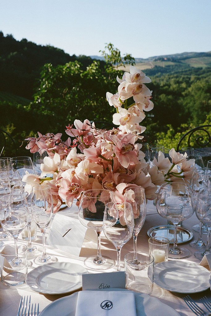 Outdoor wedding table with blush pink floral centrepiece and glassware overlooking Italian hills