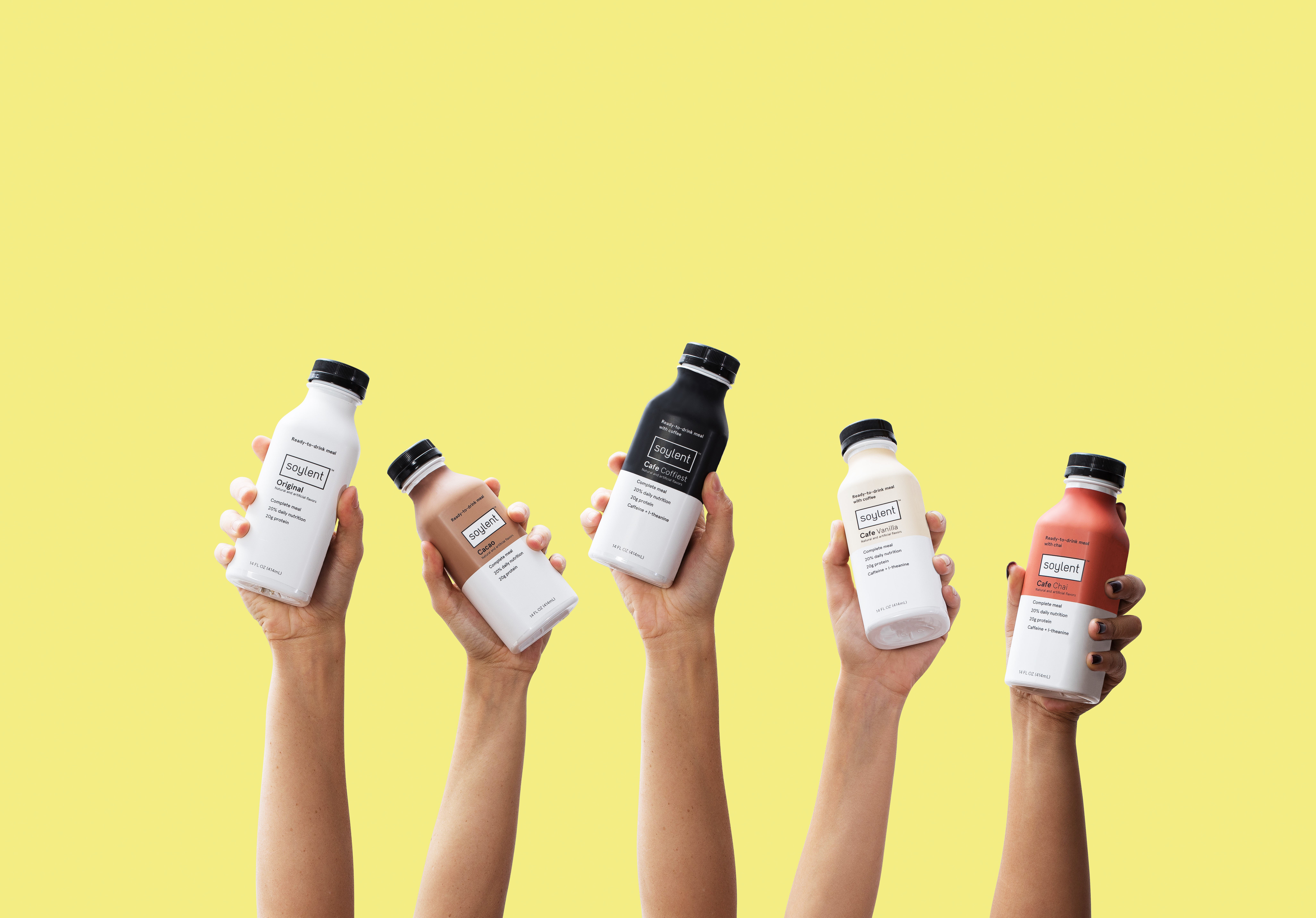 Soylent bottles being held up in the air on a yellow background