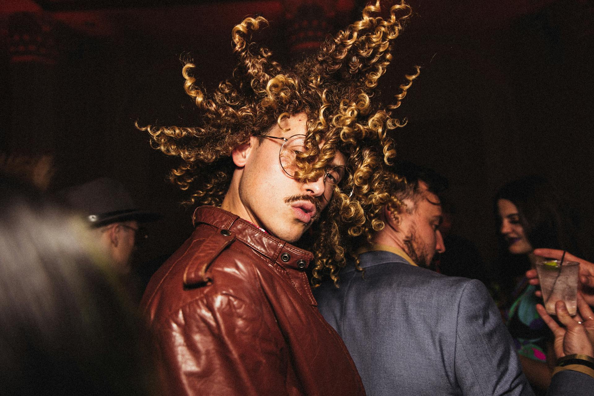 A man with voluminous curly hair and a leather jacket at a party