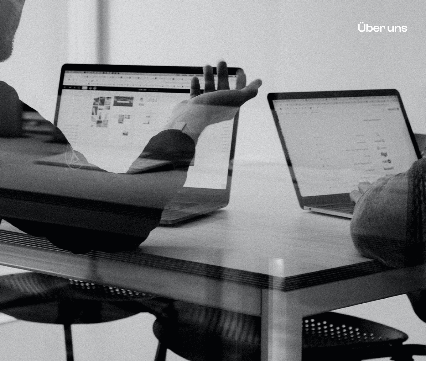 Black and white photo of two people looking at a computer screen with papers on wall
