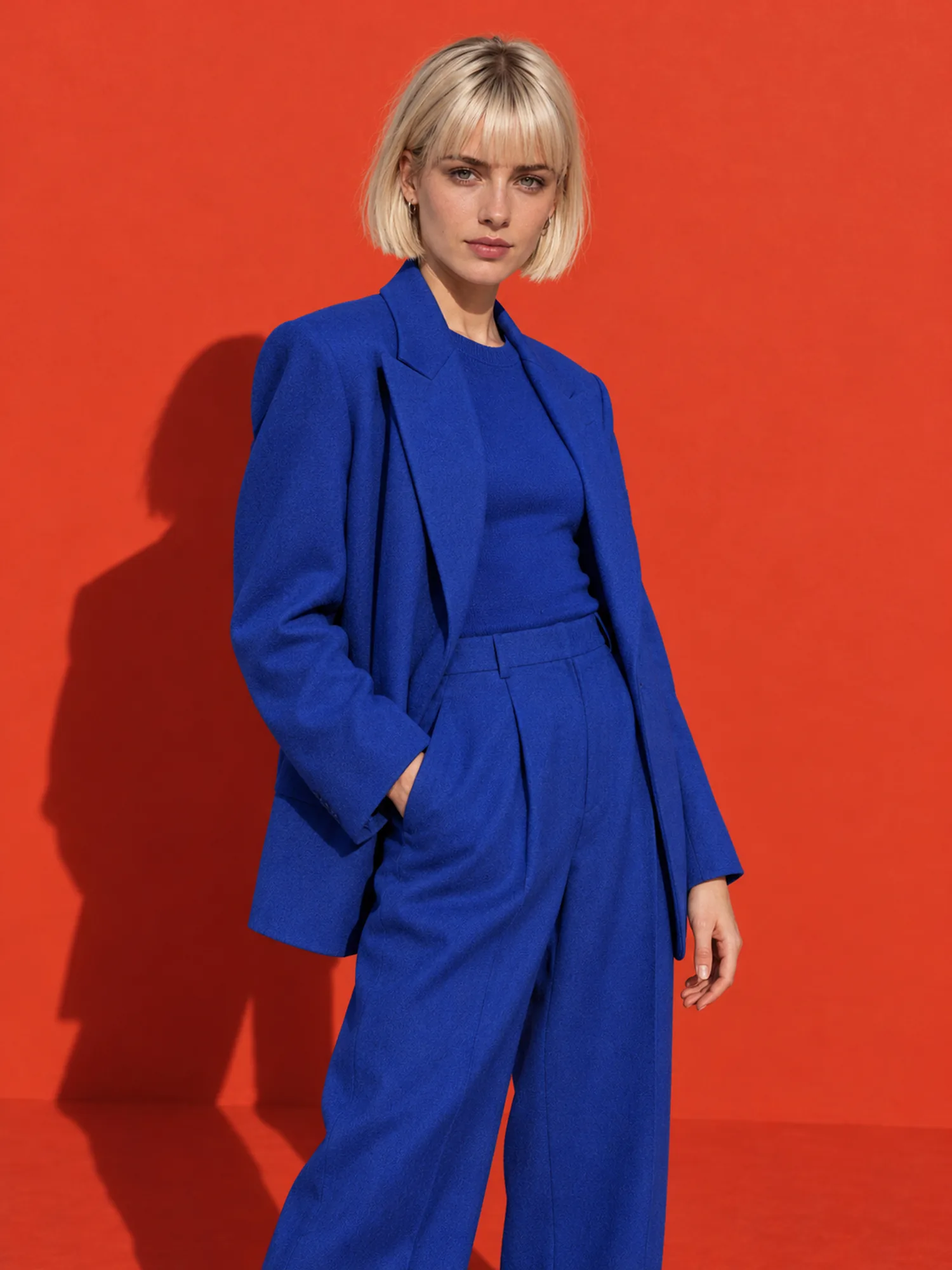 A woman with a platinum bob in a cobalt suit against a red wall