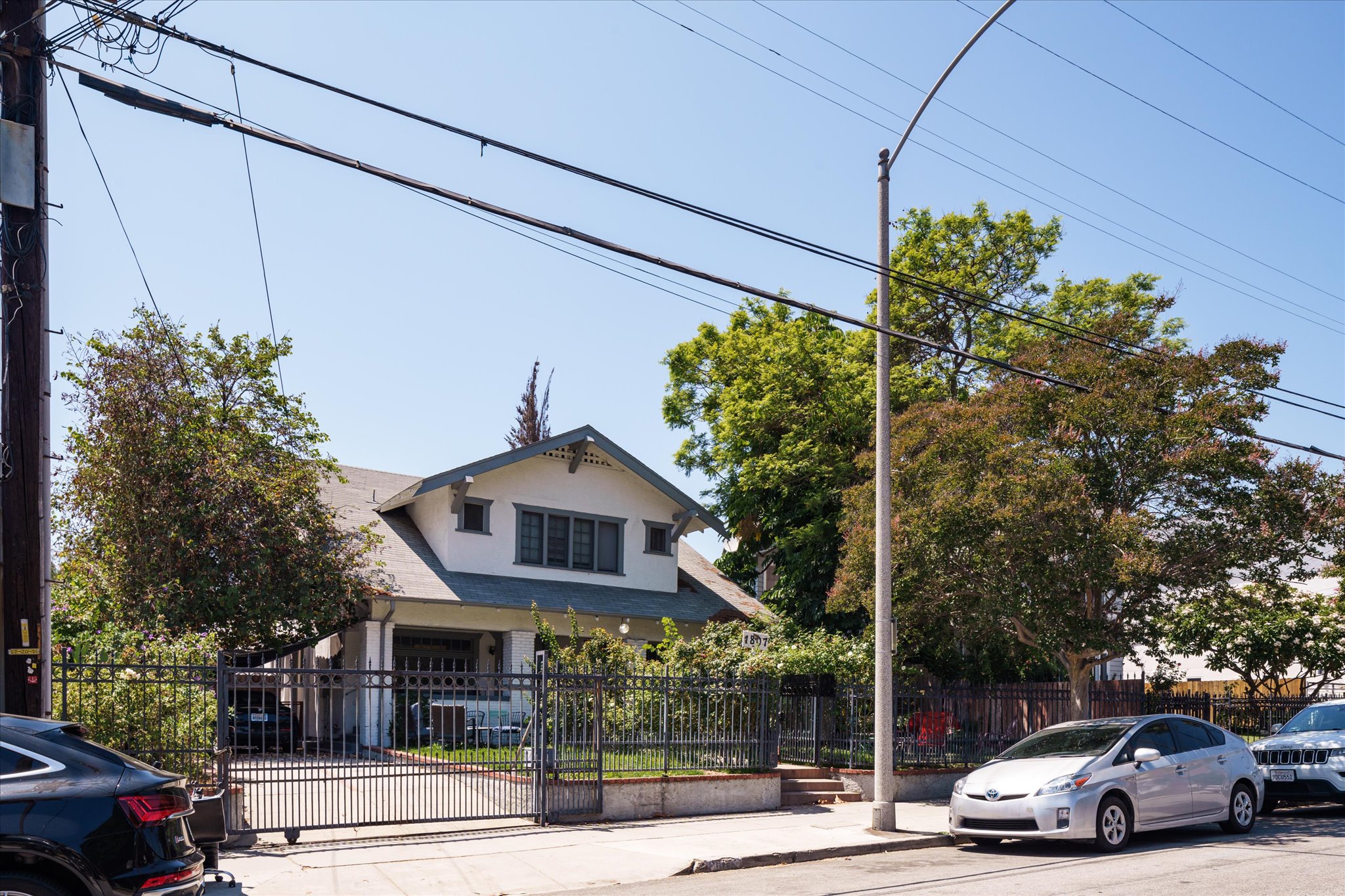 A sunny street view of a house at 1807 n van ness ave, surrounded by trees, with parked cars and utility lines in the foreground.