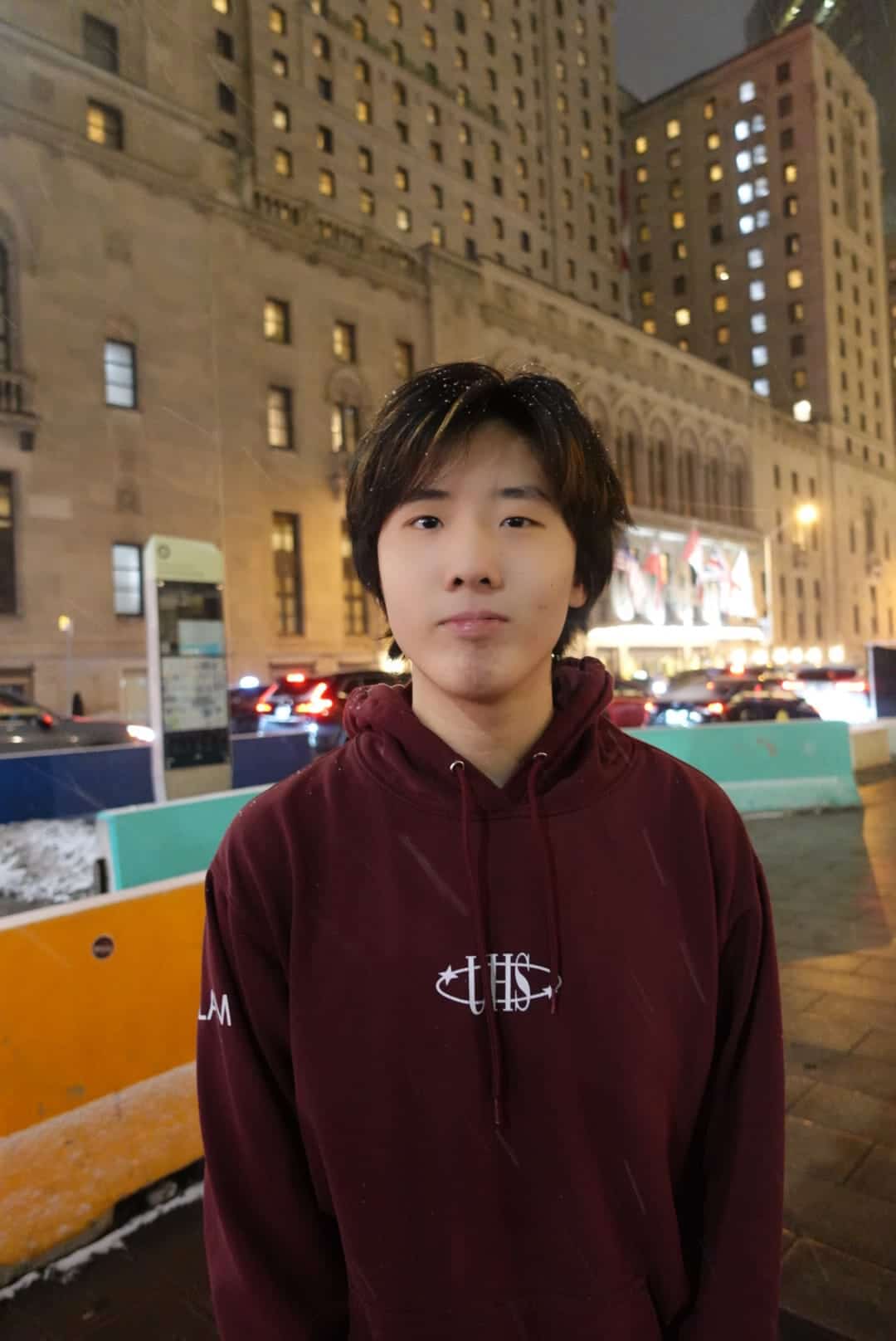 A smiling person with curly hair, wearing a leather jacket, stands in a cozy indoor setting.