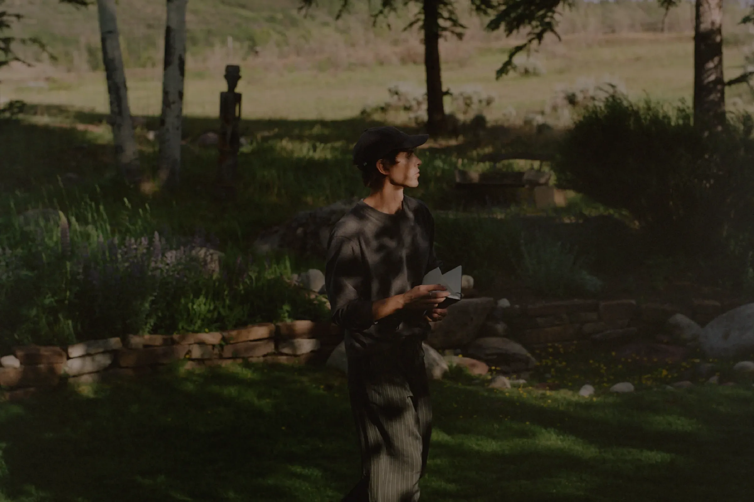 Man standing in a landscaped garden surrounded by trees and mountain vegetation.