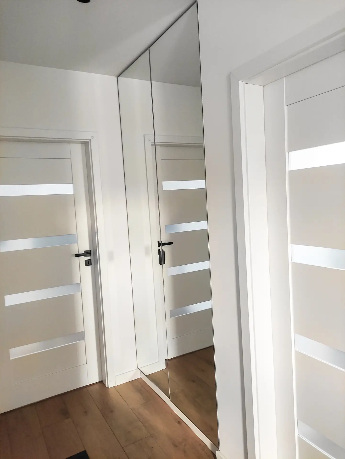 Nowoczesna biała szafa wnękowa ze zintegrowanymi frontami i drzwiami obok.