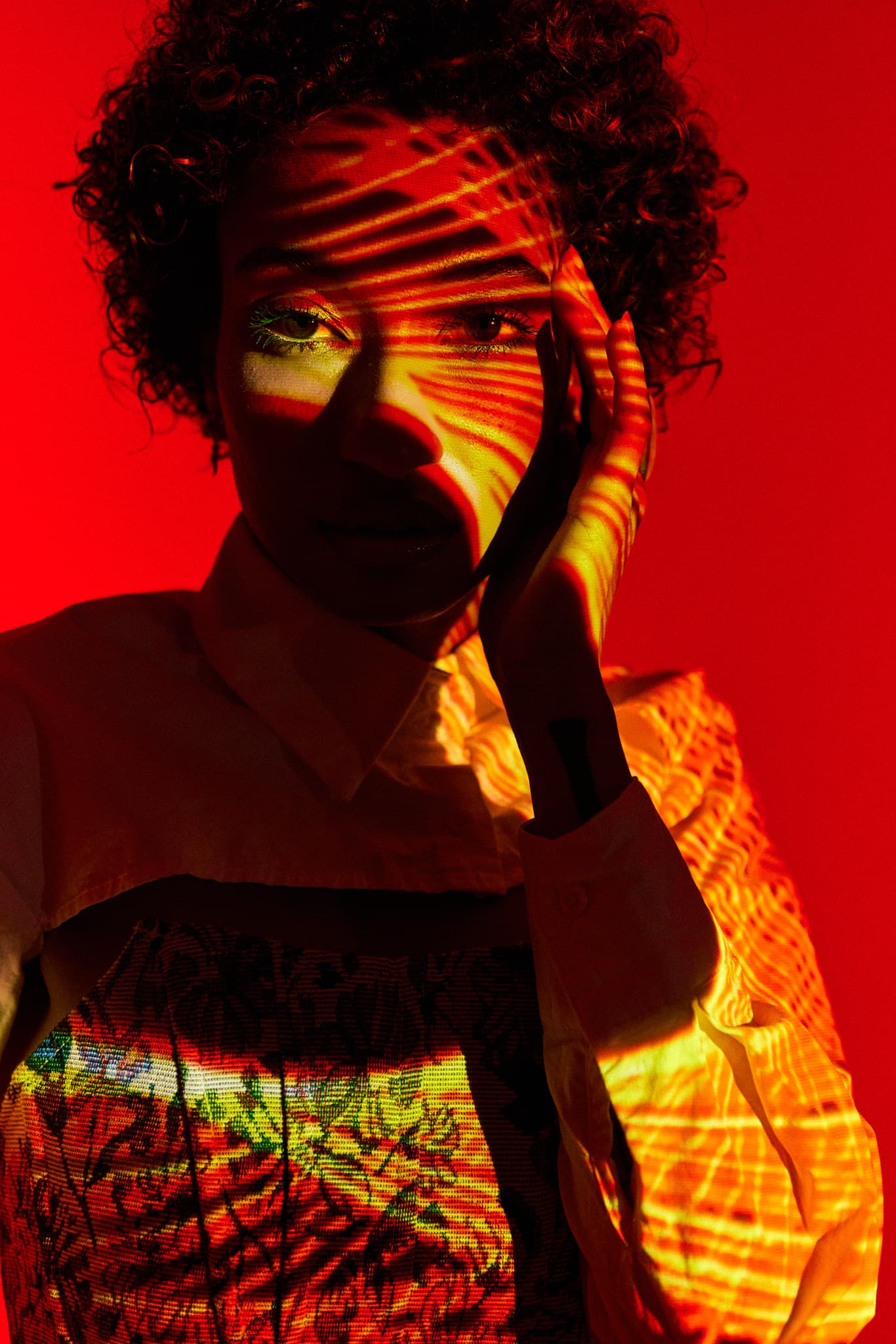 A model with curly hair is illuminated with red light and shadow patterns across her face at Revelator Studio, a natural light photography studio in Shreveport.