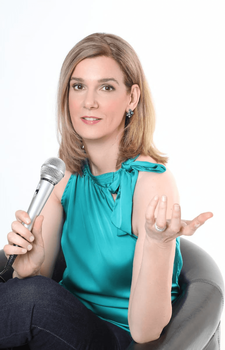 Vocal Coach Danielle Zuber im professionellen Auftritt. Nahaufnahme mit Mikrofon und türkisfarbenem Oberteil, strahlendes Lächeln.