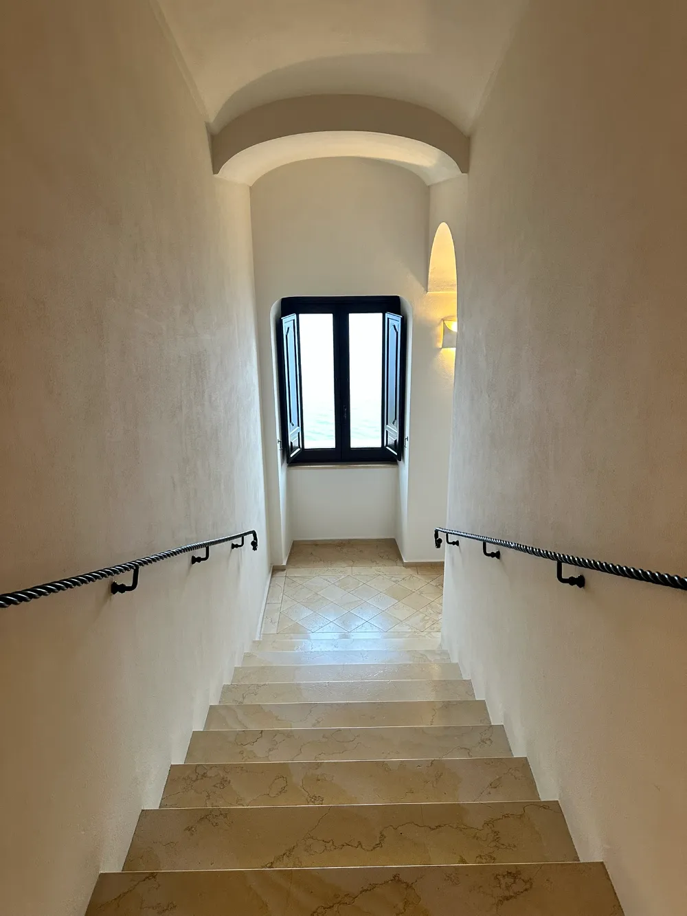 A narrow vaulted stone staircase at Monastero Santa Rosa leading up towards a window.