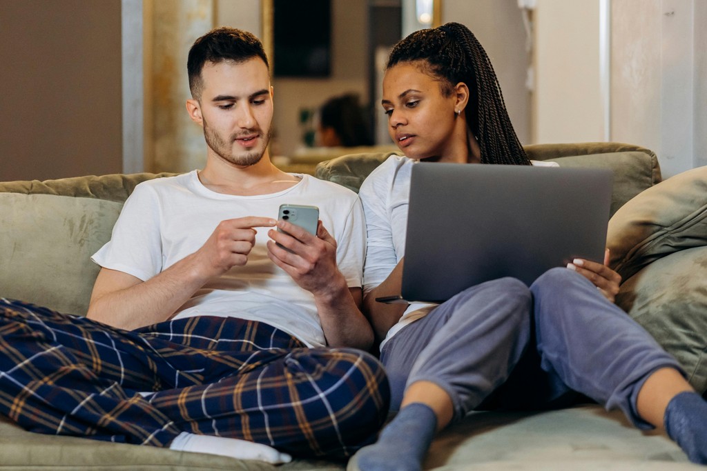 A Woman Holding a Laptop Beside a Man Holding a Cellphone