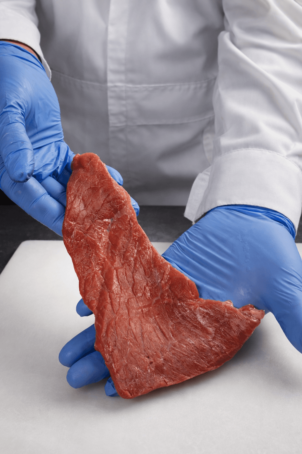 A person in an apron uses a wooden peel to place a freshly baked loaf of artisan bread into a rustic, wood-fired oven, with a flickering fire visible inside, set against the backdrop of a sunlit kitchen.