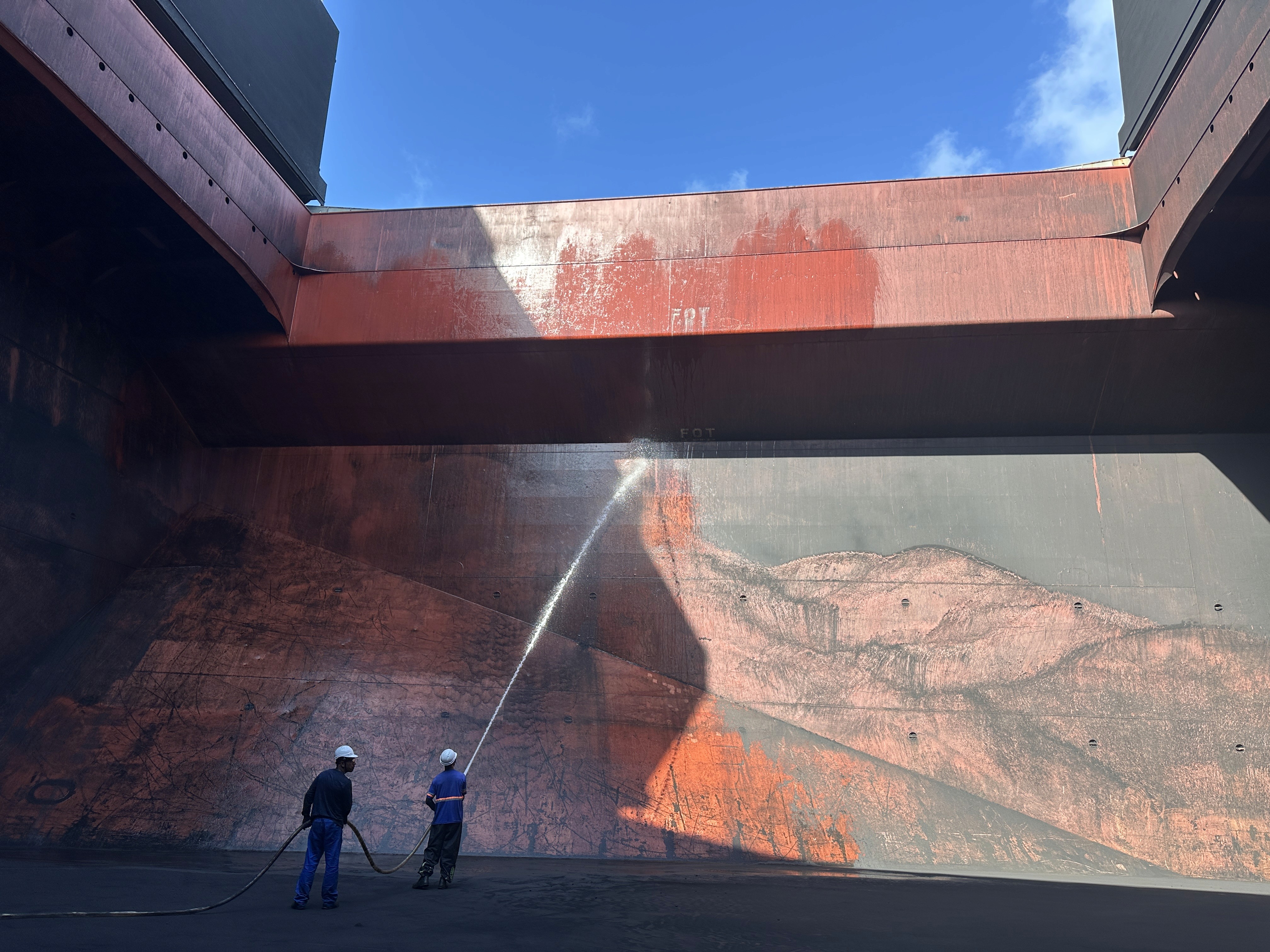 Seachios® Marine Services team performing high-pressure cargo hold cleaning inside a box-shaped bulk carrier hold at Cabedelo, Brazil, removing red clinker residues to achieve grain-ready standards before loading in Santos.