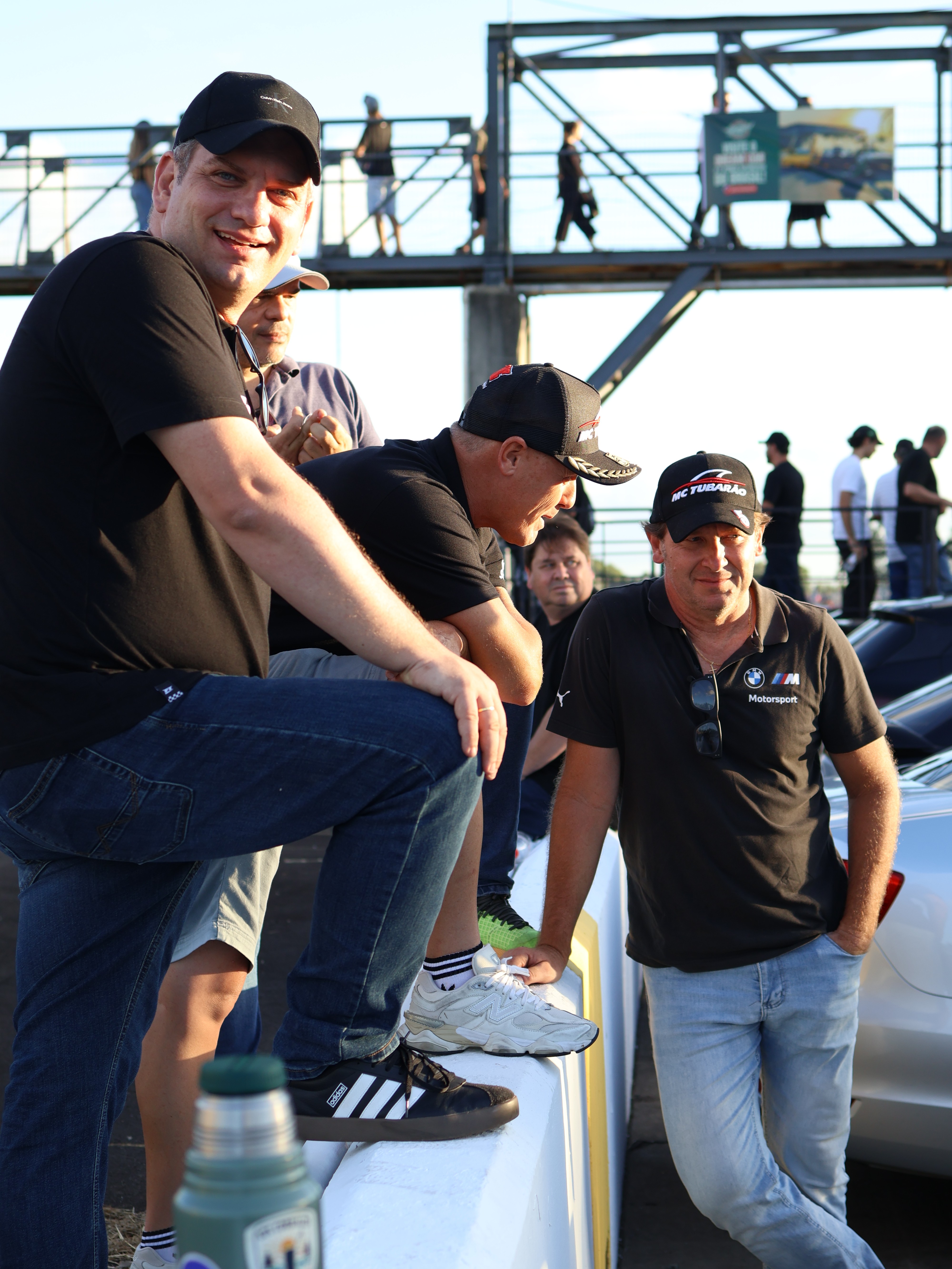 Two people in a workshop, one standing and smiling while the other leans over a car, working on it.
