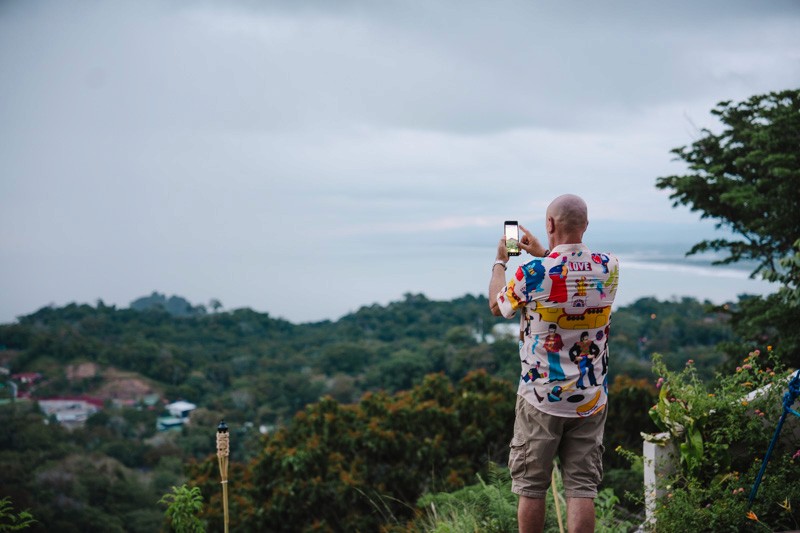 Guest taking a photo of the panoramic lush rainforest and ocean view from a hillside vantage point.