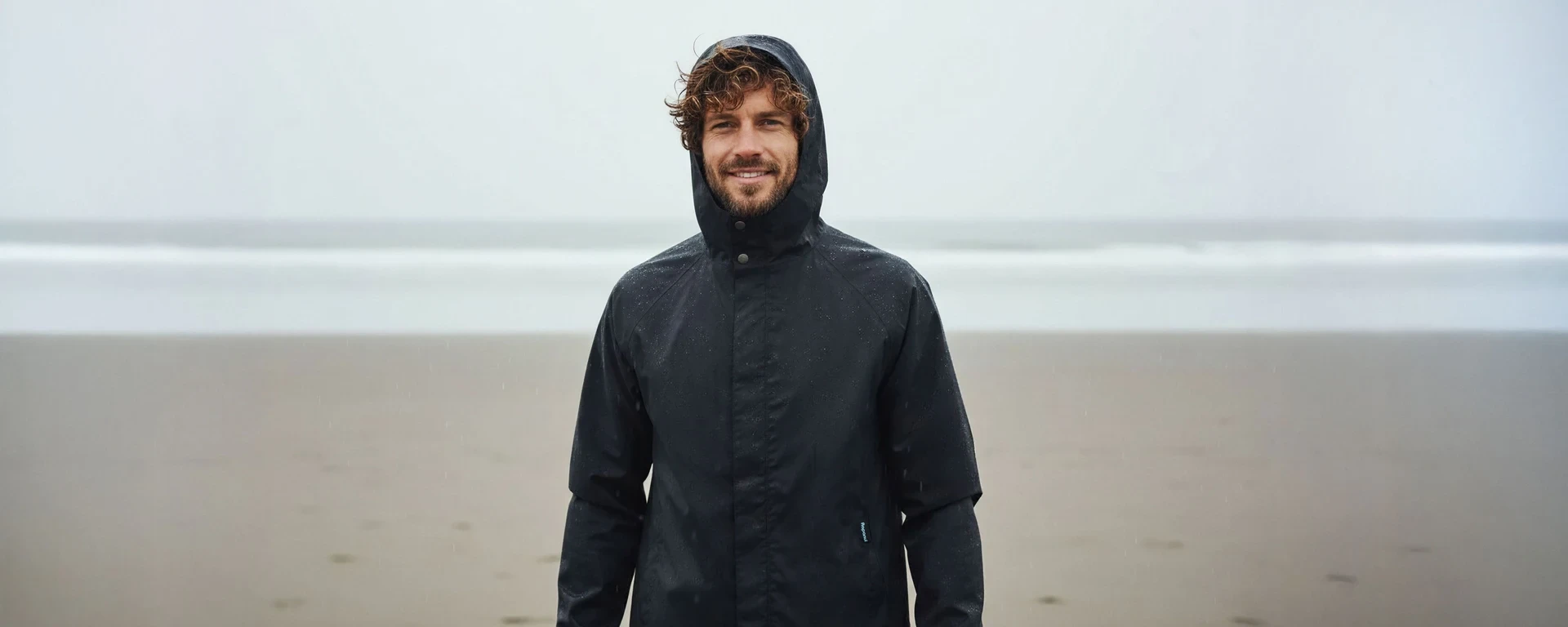 Fashionable man in a cream quarter-zip pullover and sunglasses standing against a minimalist concrete wall.