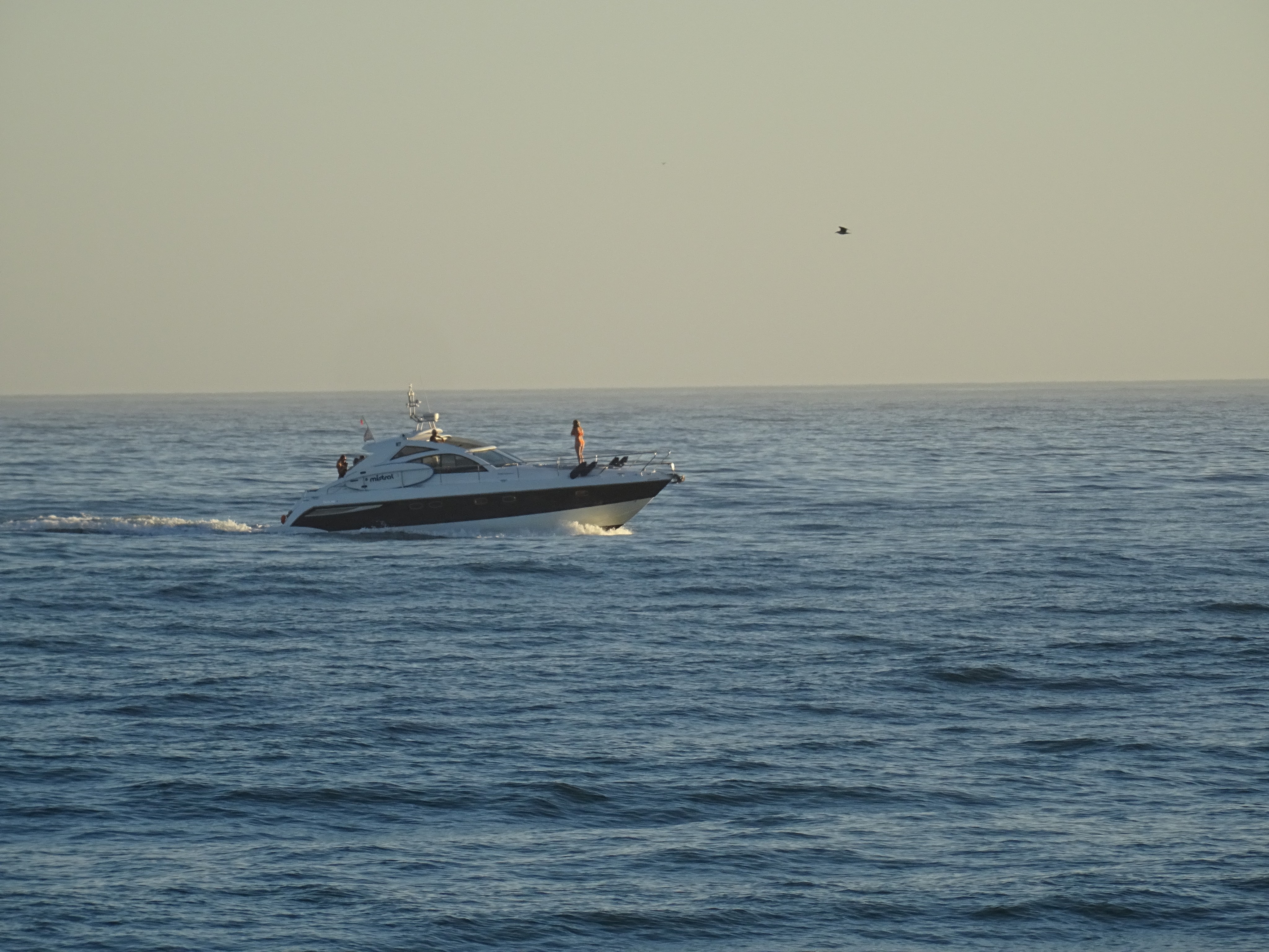 Small boat sailing on calm blue water under a pale evening sky.