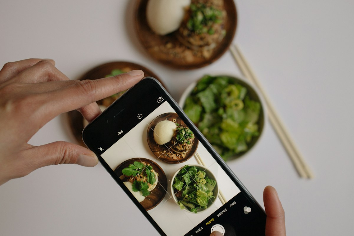 A person photographing a plate of healthy vegetables with a smartphone food-logging app.