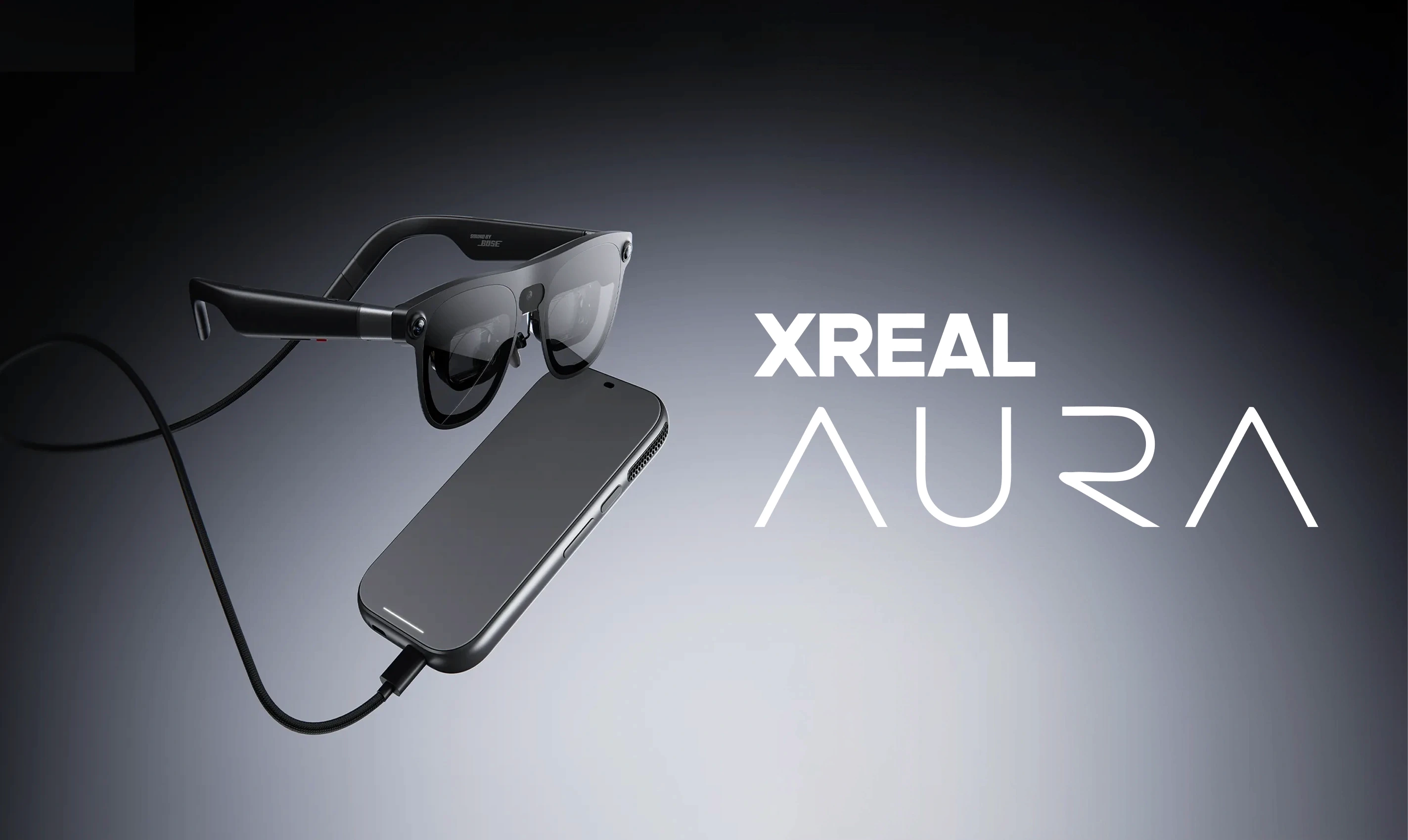 XREAL Aura glasses tethered by a braided cable to a black compute puck, floating against a grey gradient beside the XREAL Aura wordmark.