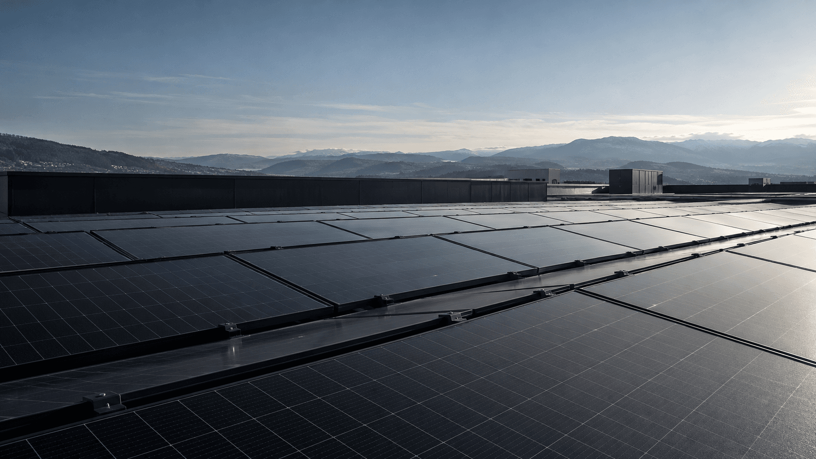 Solar modules on a flat roof at dusk, with hills in the background