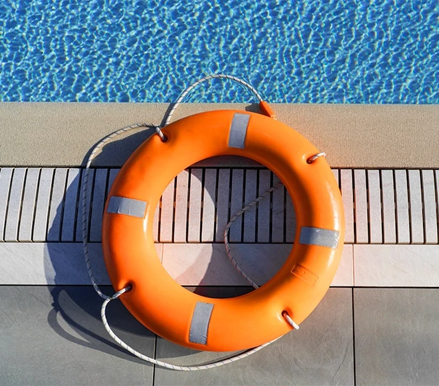 An orange lifebuoy ring with a rescue rope sitting on the concrete edge of a swimming pool, representing catastrophic injury claims and drowning emergency investigations by Schwinghamer Law in Stockton.