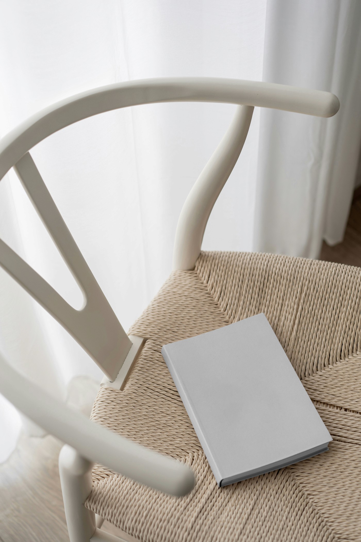 Mockup of a purple hardcover book resting on a woven seat of a minimalist wooden chair. The soft natural lighting and neutral tones create an elegant, cozy setting, ideal for showcasing book designs.