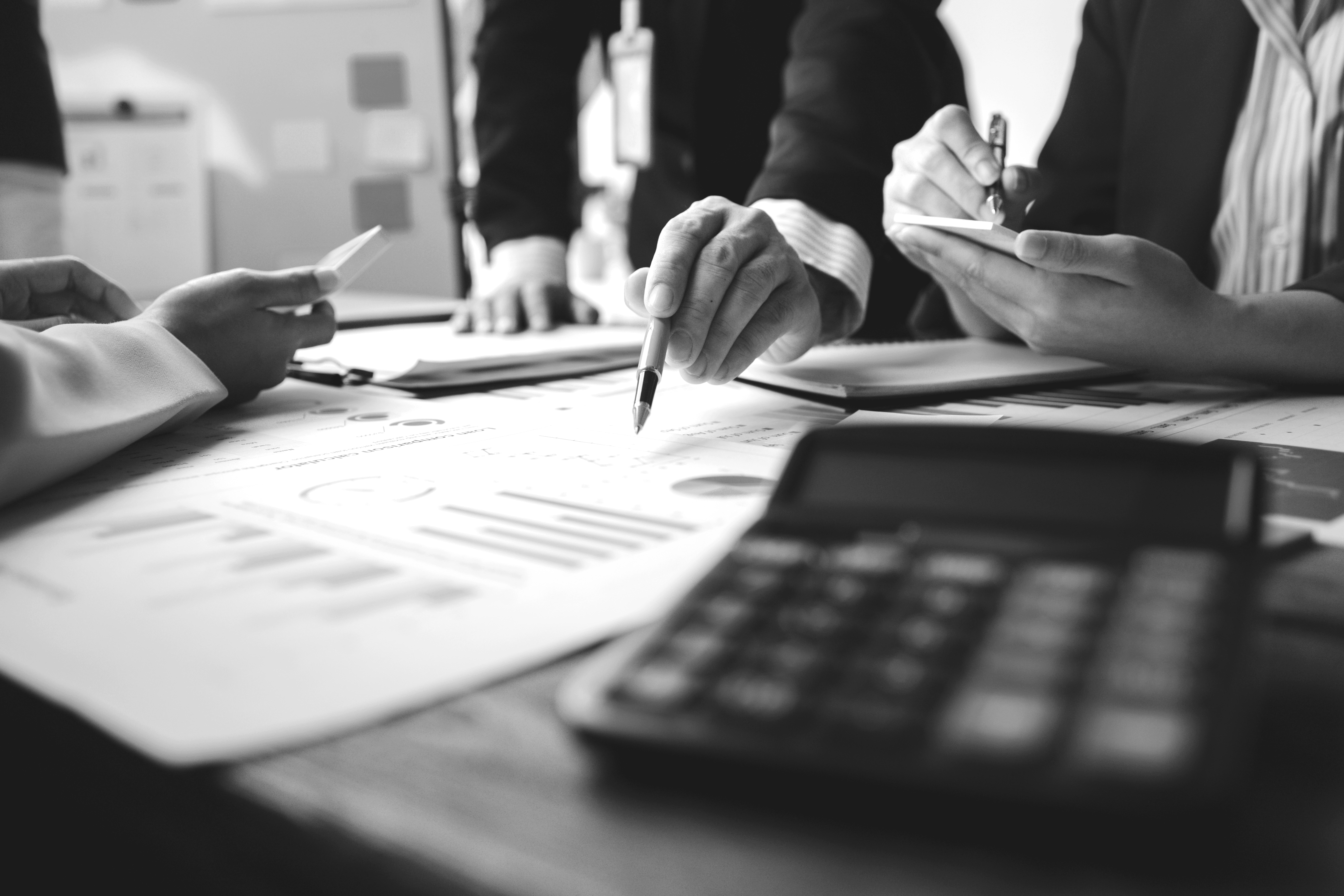 Black and white image of people working at a table with laptops, showing hands gesturing during discussion of digital content displayed on screens, with fabrica® logo in the corner.