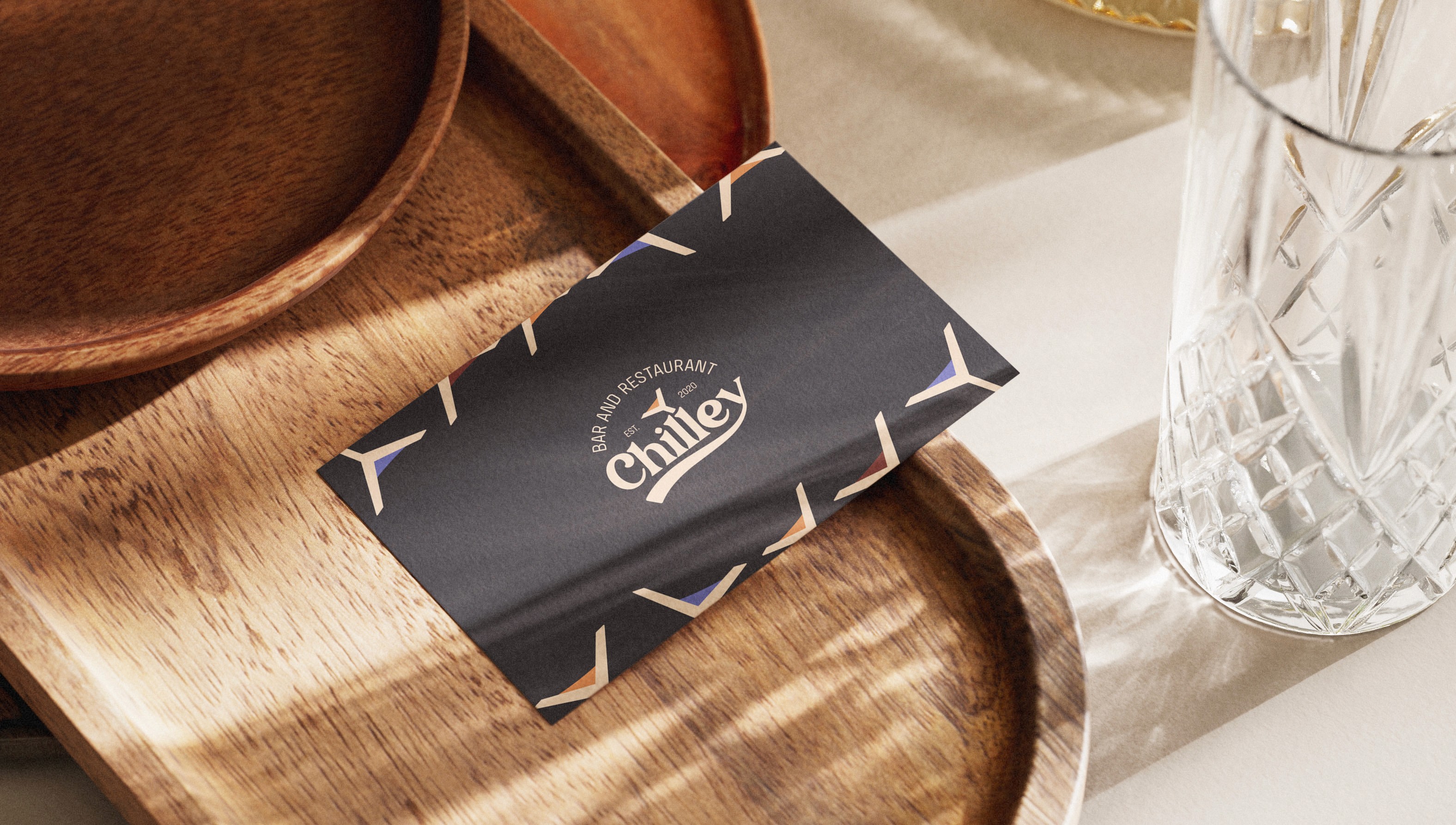 Chilley business card with a martini glass pattern resting on a wooden tray next to a crystal glass.