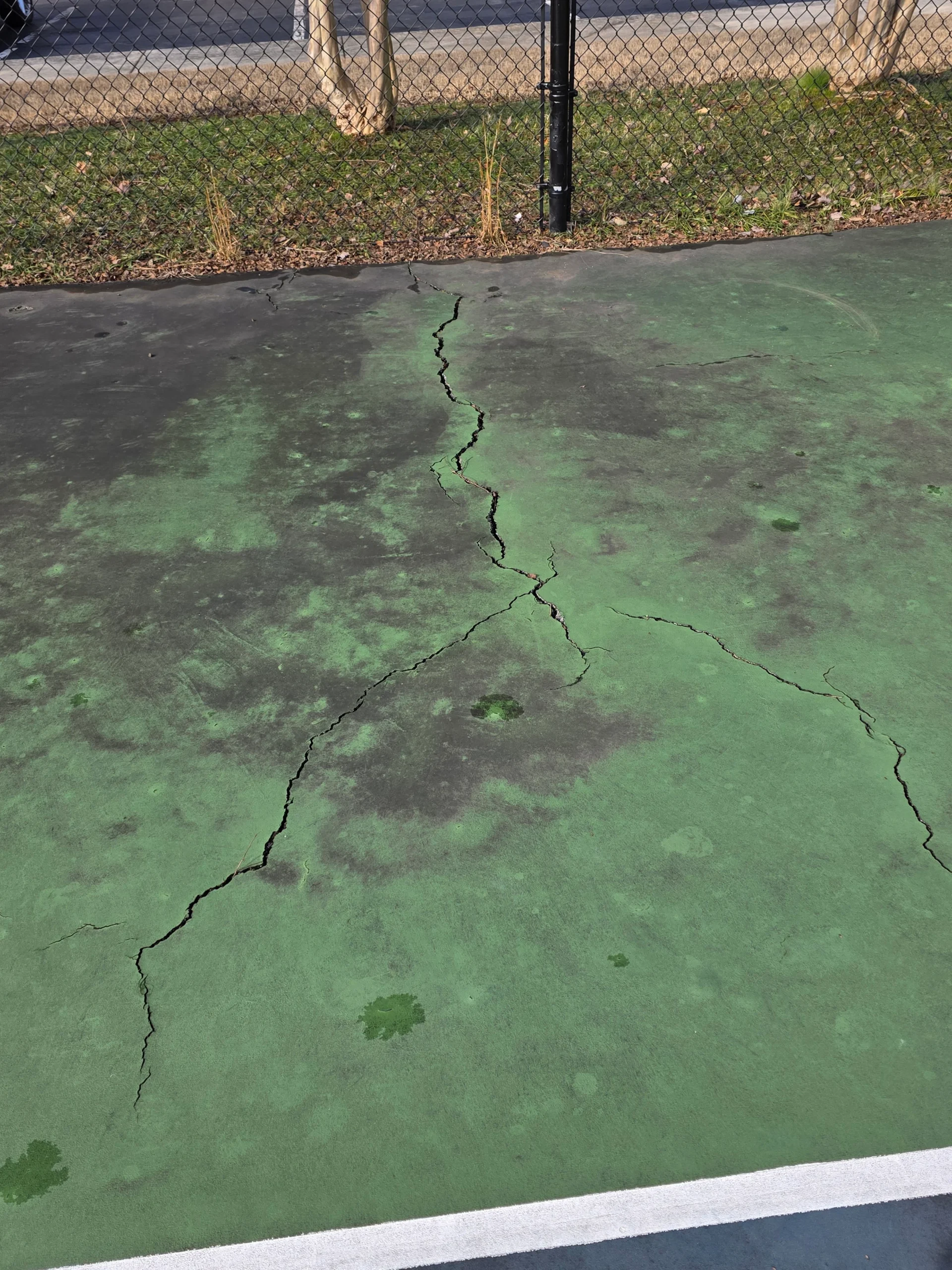 Branching cracks in faded green out-of-bounds area before resurfacing at Weston Ranch in Madison, AL