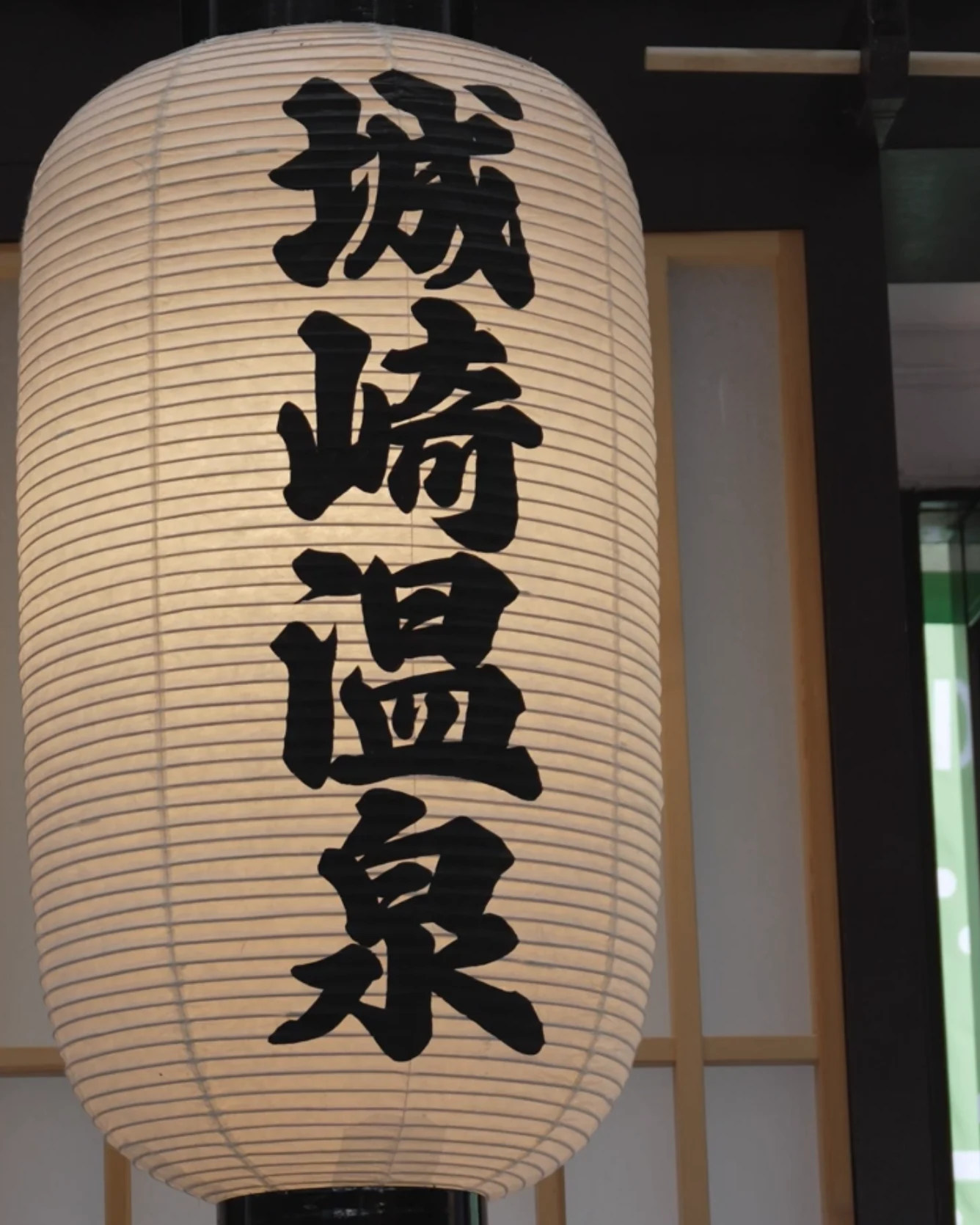 A tall paper lantern printed with the name Kinosaki Onsen, lit at an entrance.