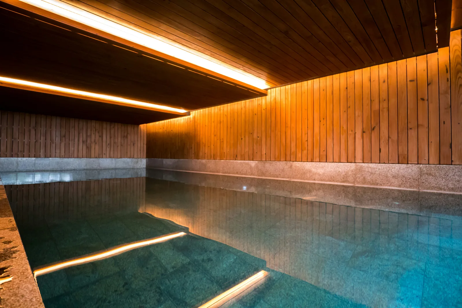 An indoor hot pool lit by warm strip lights under a wooden ceiling