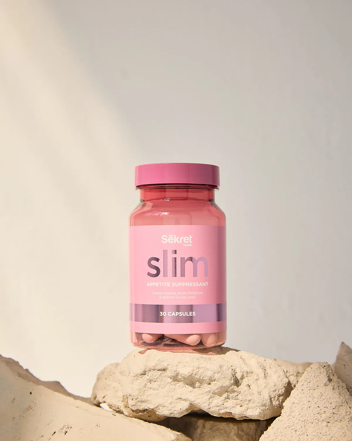 A bottle of Sēkret Slim capsules standing on a rough stone in warm light
