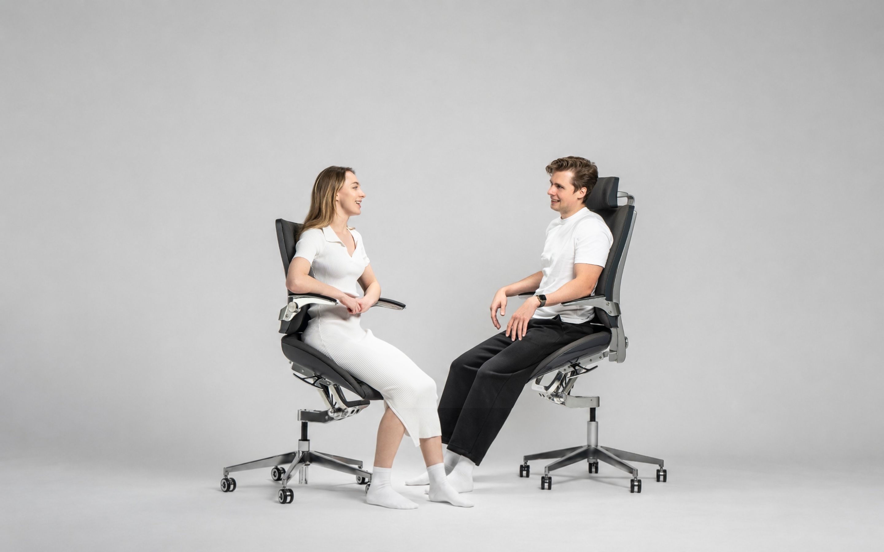 Two professionals work comfortably across a shared desk while seated in Levitask Vision ergonomic chairs.