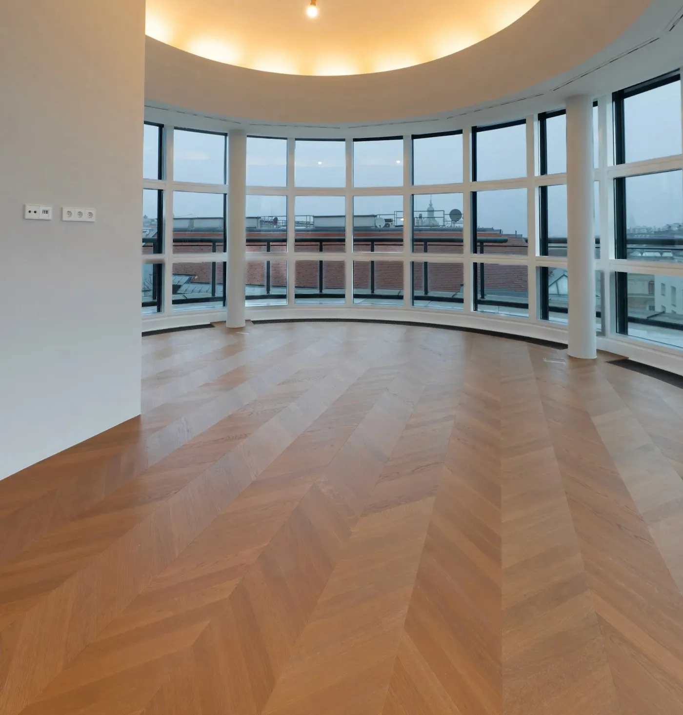 Großer Wohnraum mit gebogener Fensterfront und hochwertigem Chevron-Parkettboden.