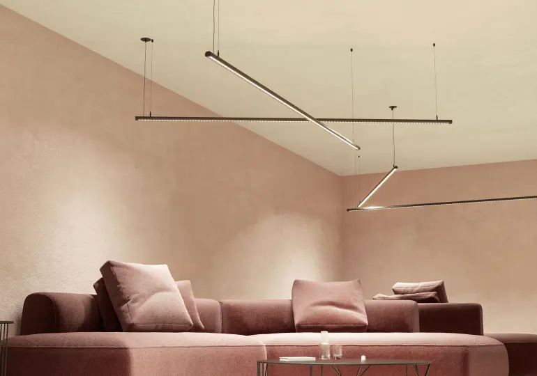 Sala moderna con sofá rosa, cojines a juego y lámparas colgantes LED de Beneito Faure, paredes rosadas y mesa de centro minimalista