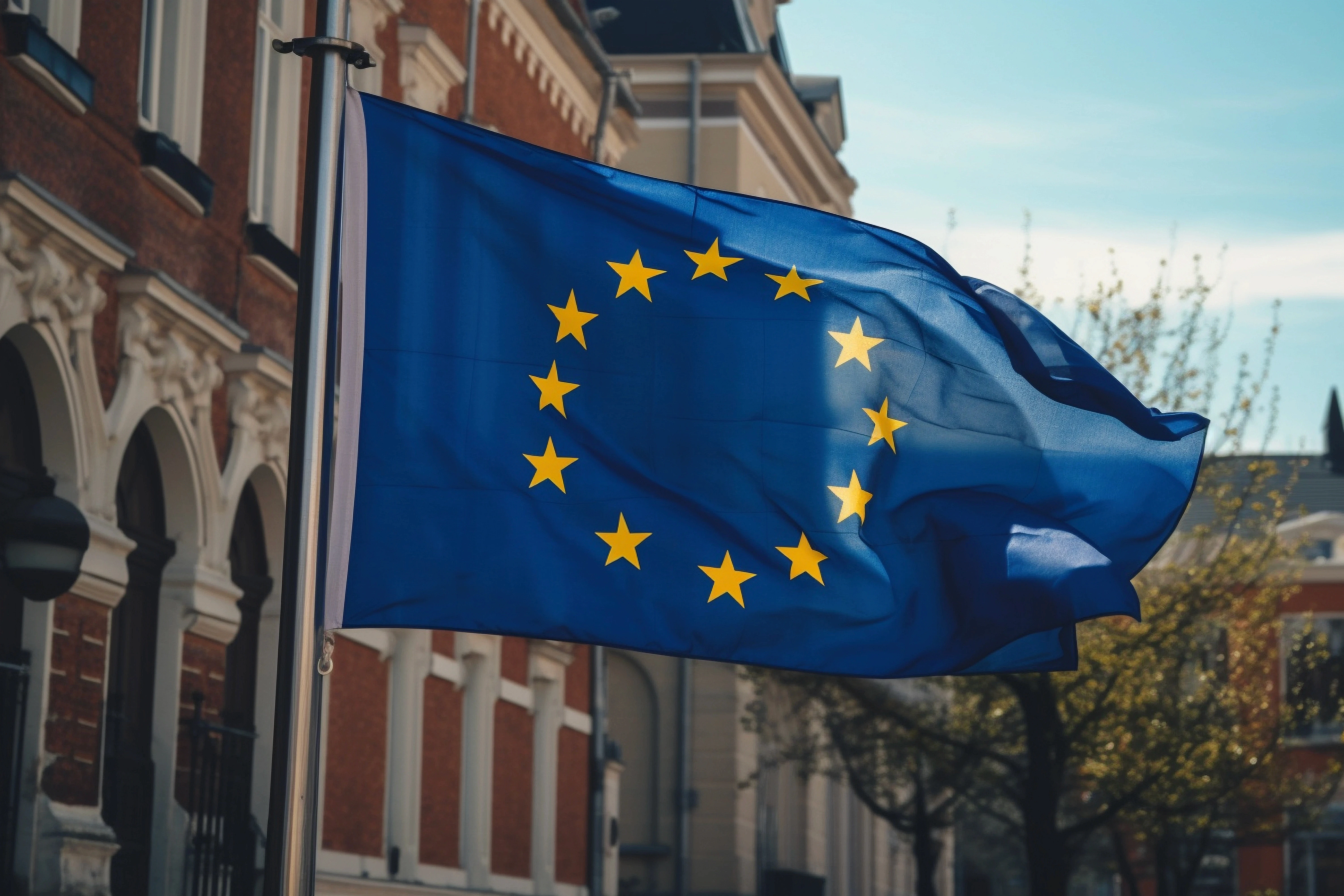 European Union flag waving in front of a red brick building on a clear day