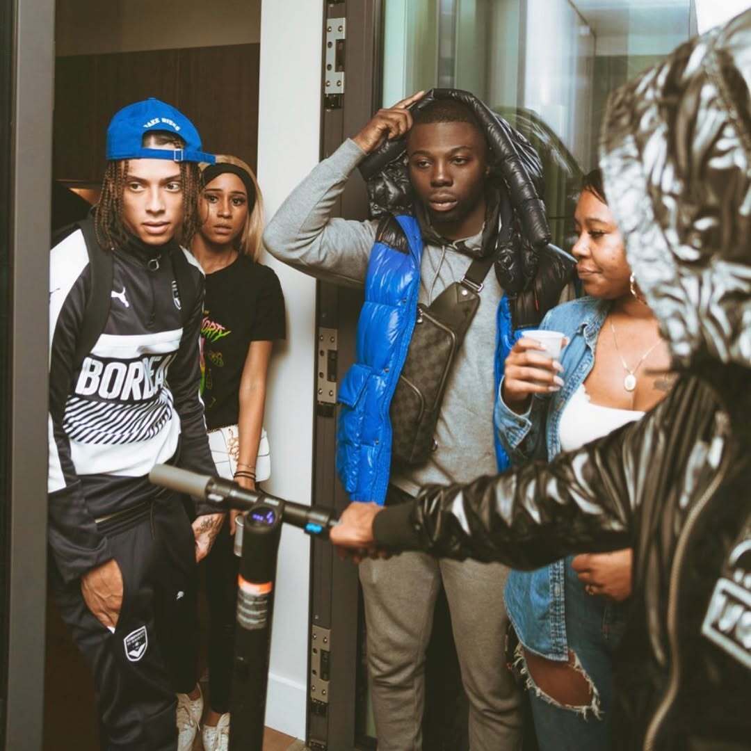 A group of friends in casual streetwear gathered at a building entrance, reflecting the artist’s journey from early bedroom recordings to global studios and authentic music culture.