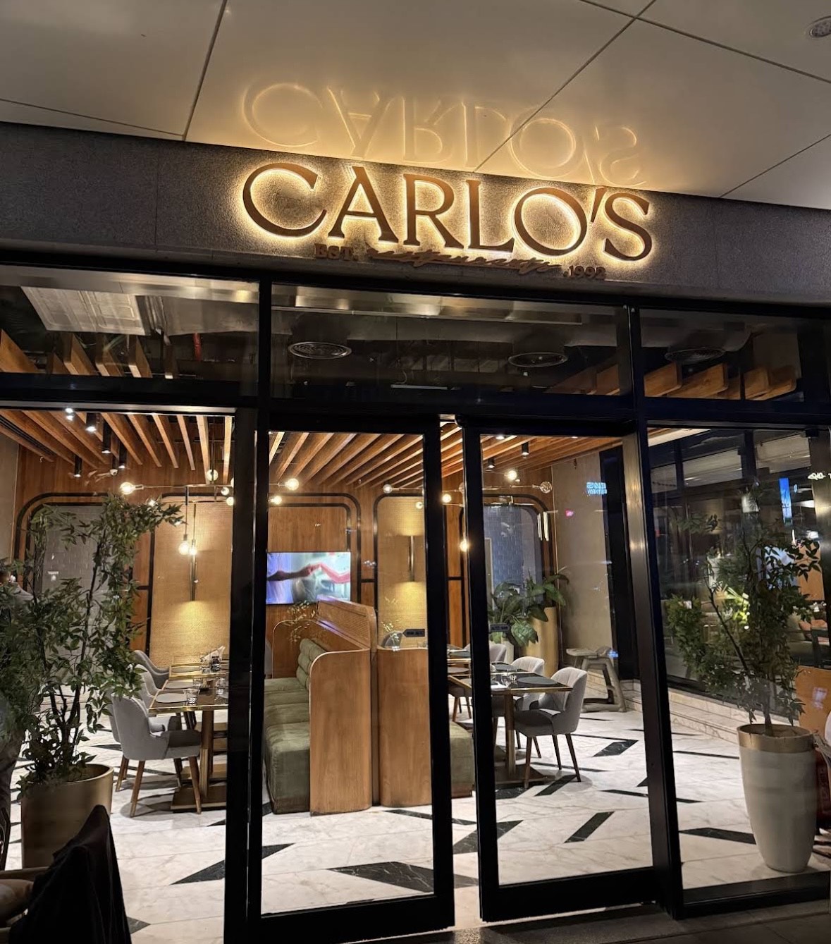 An overhead shot of a large oval plate featuring sliced, roasted duck, half glazed with a sauce, served over two thin pancakes and alongside steamed bok choy, surrounded by small bowls of condiments like scallions, sauce, salt, and carrot shreds.