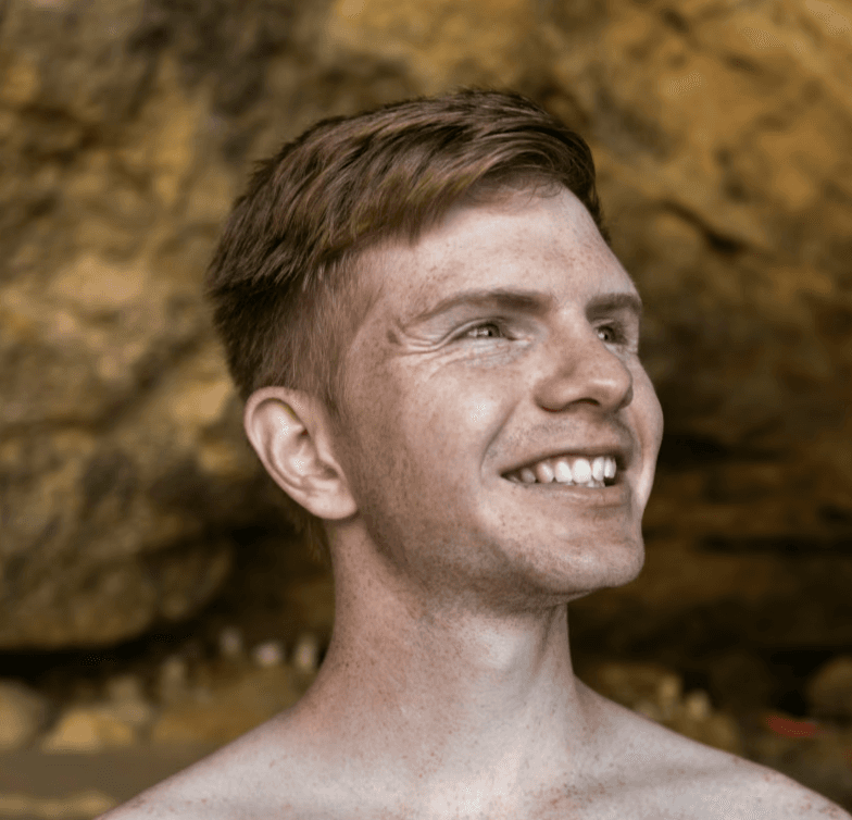 a young man wearing glasses standing in front of a mountain