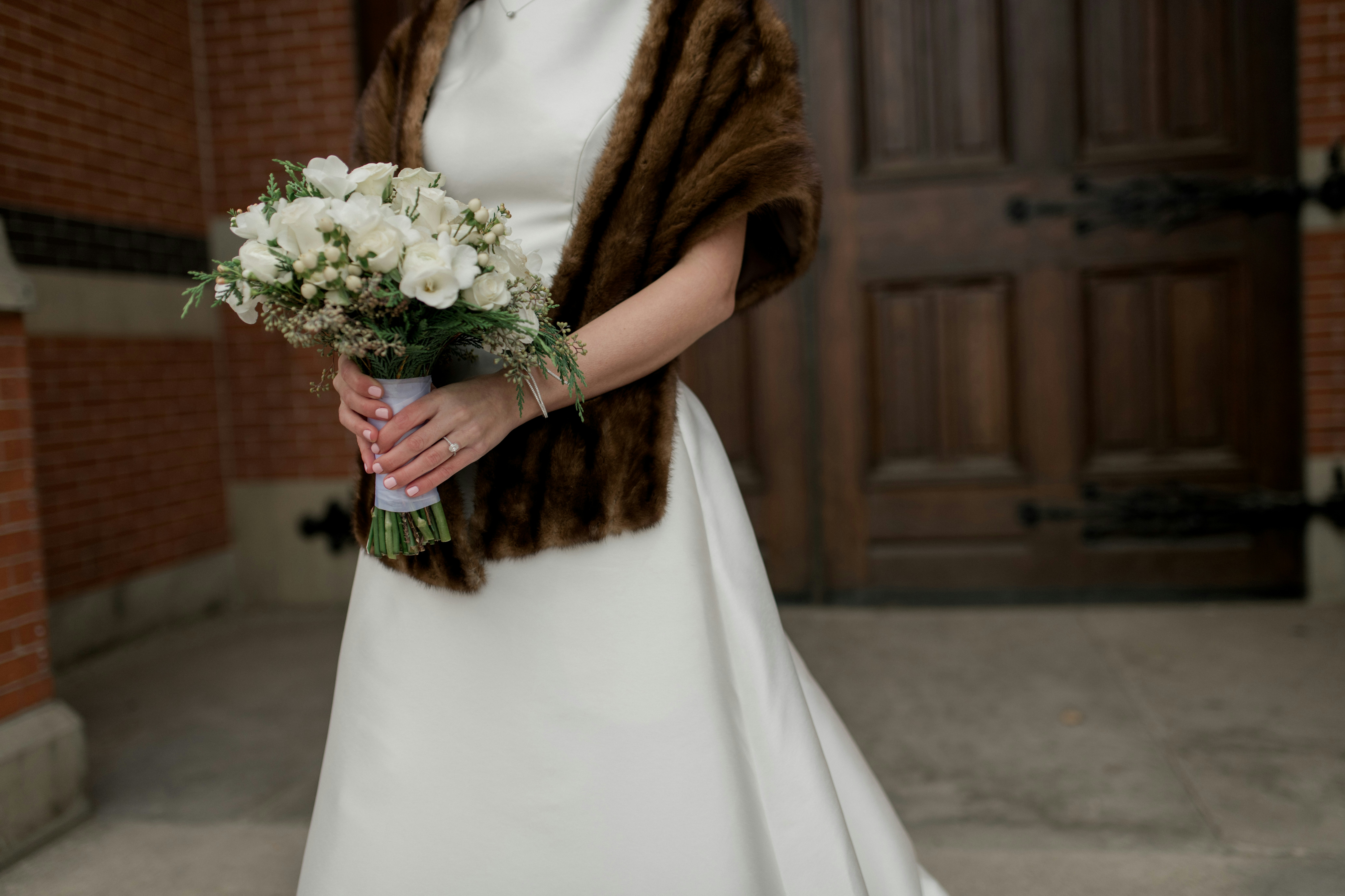Bride holding a bouquet with a brown fluffy shawl draped over her shoulders.