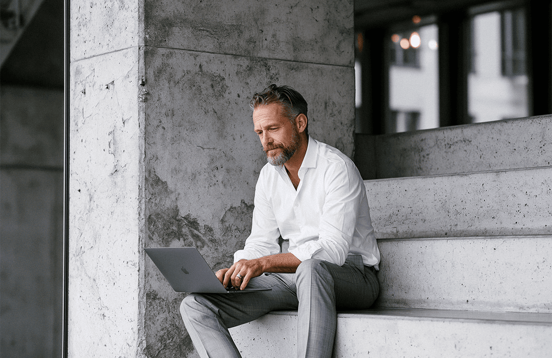 Blog post Inspira. Advogado trabalhando no laptop sentado na escada externa de um escritório moderno de concreto.