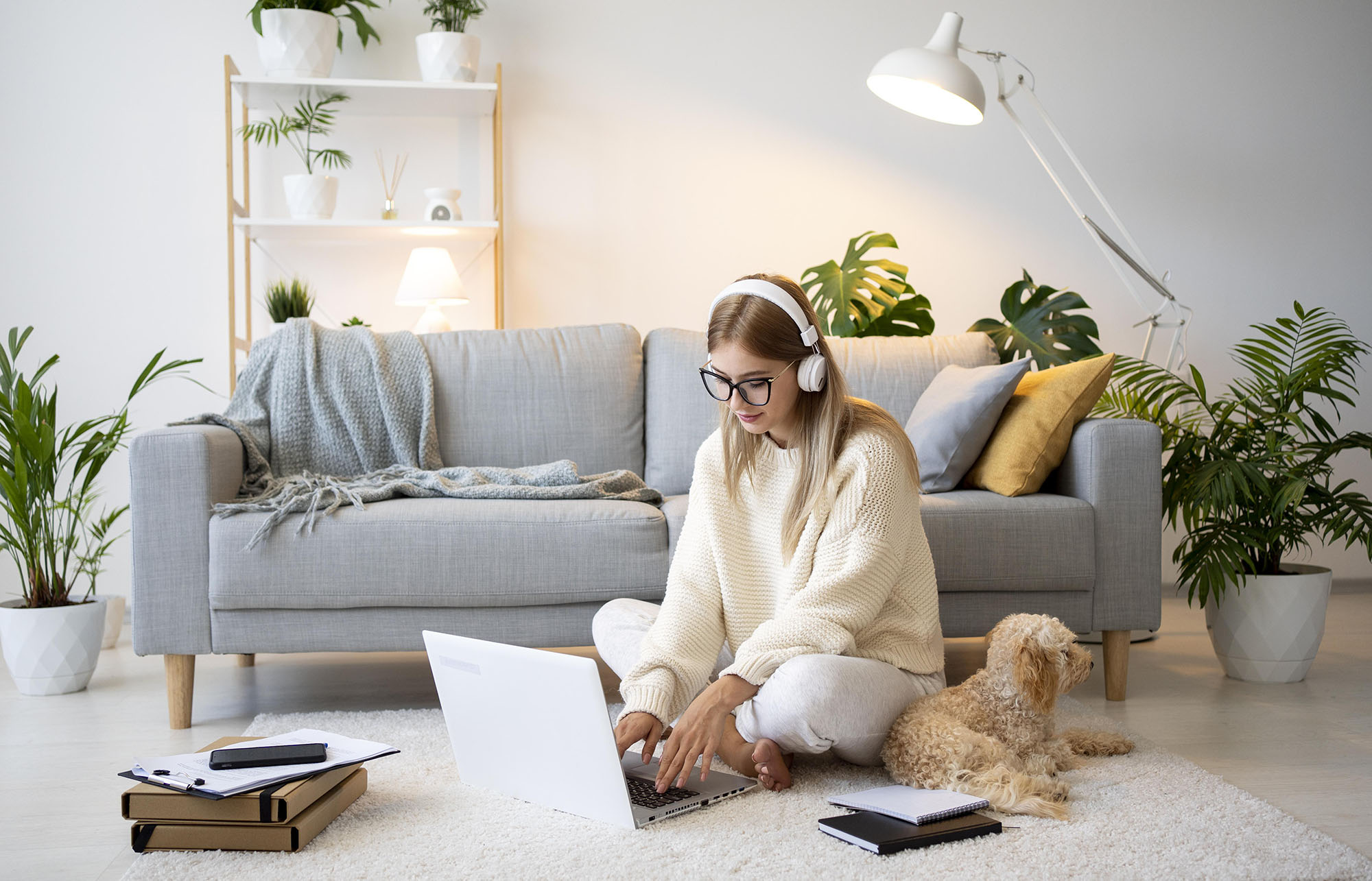 Young person working from home, sitting on floor in living room near sofa with laptop on the floor