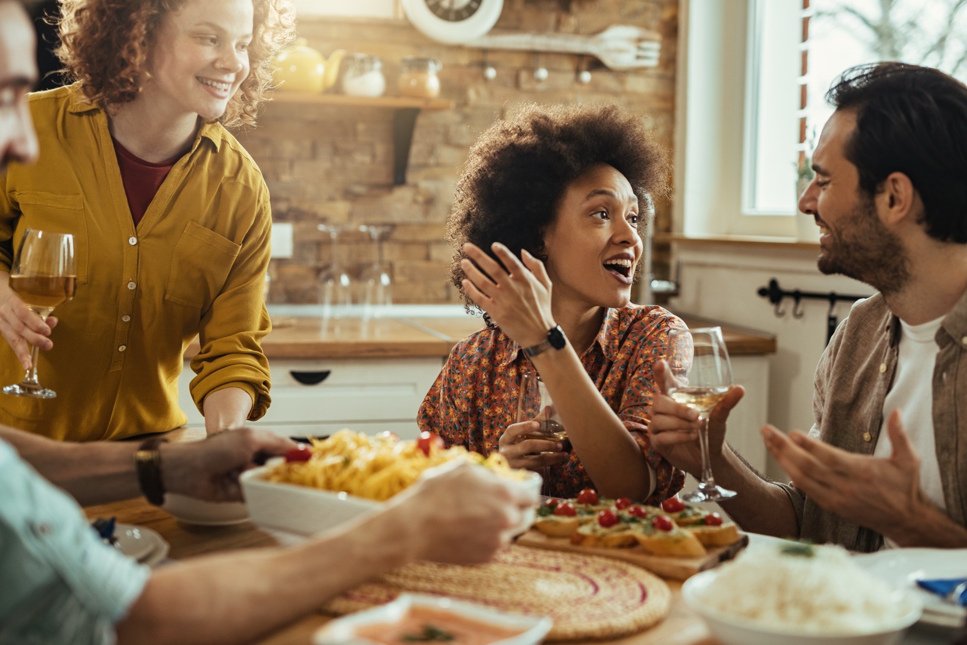 Three young adults gathered around a dining table sharing food and laughing in a cosy flat, depicting sociable student living.