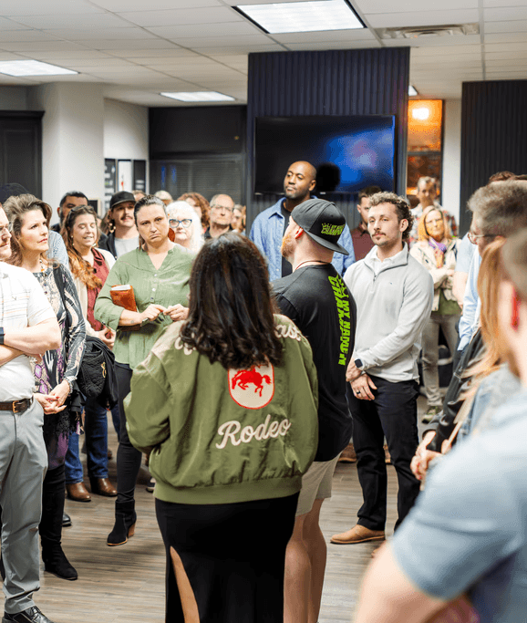 A speaker on stage, illuminated against a dark background, gestures while addressing an audience.