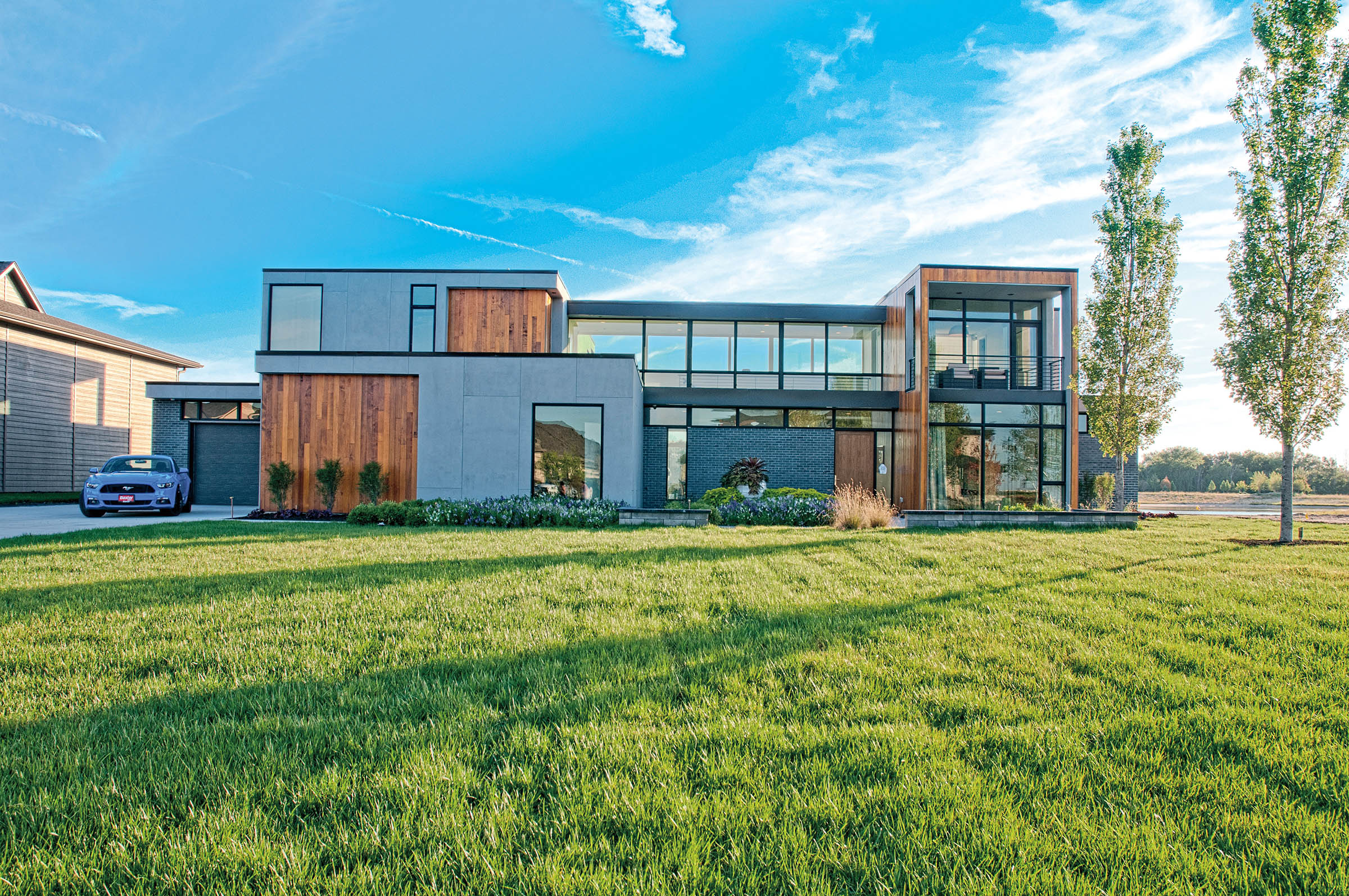The foreground features a vast, neatly manicured green lawn, with a small garden bed of lavender and ornamental grasses bordering the base of the house.