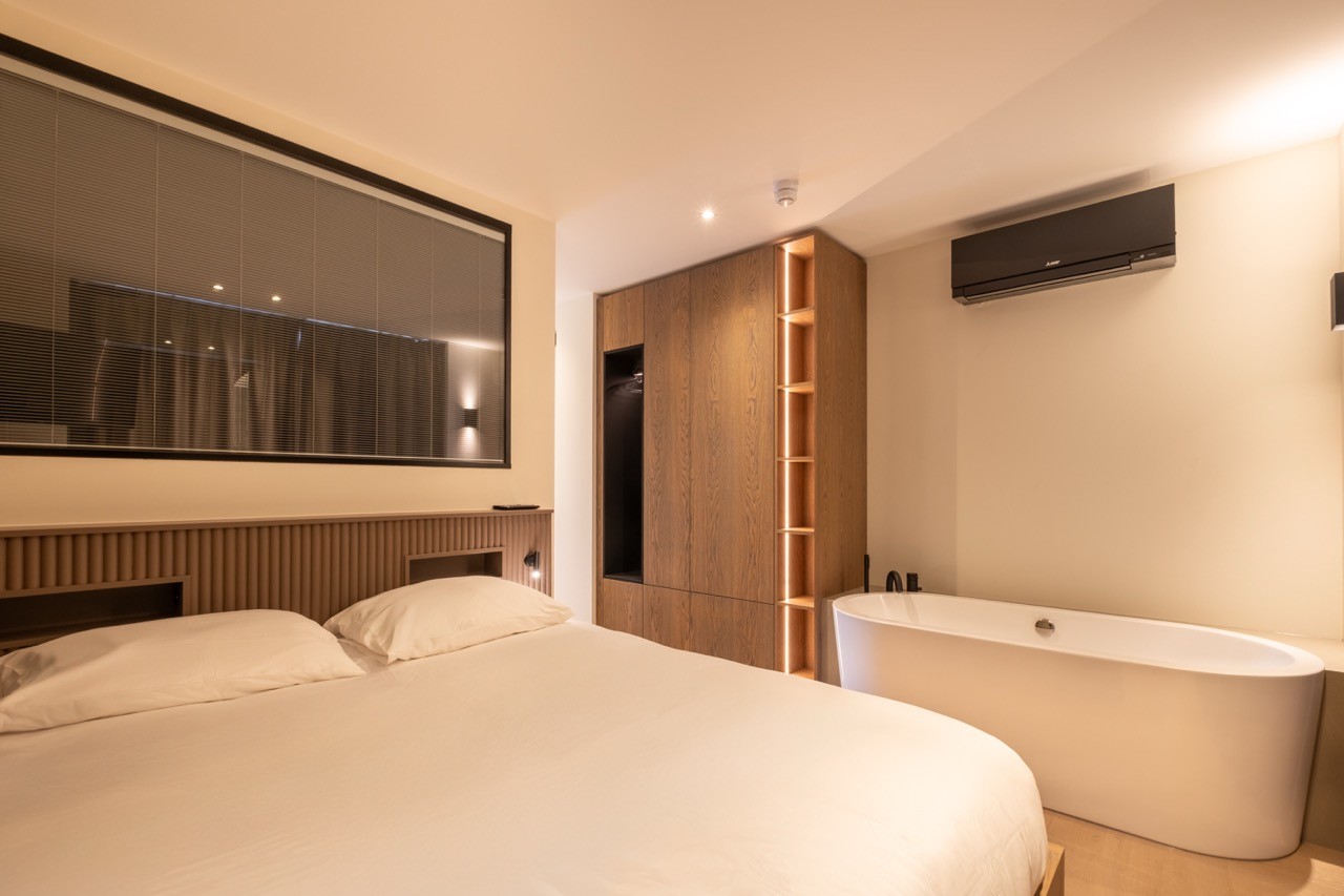 Luxe slaapkamer van Suite met vrijstaand bad, houten kast en grote spiegelwand.