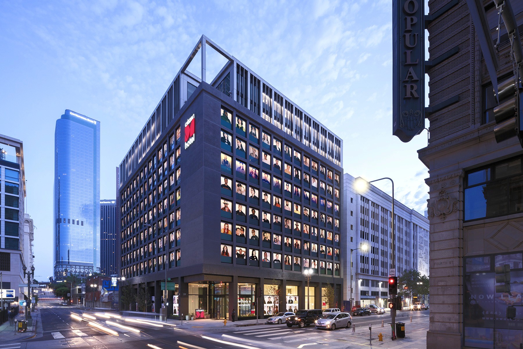 A vibrant hotel with a red sign, featuring ground-level amenities and artwork displayed in each window.