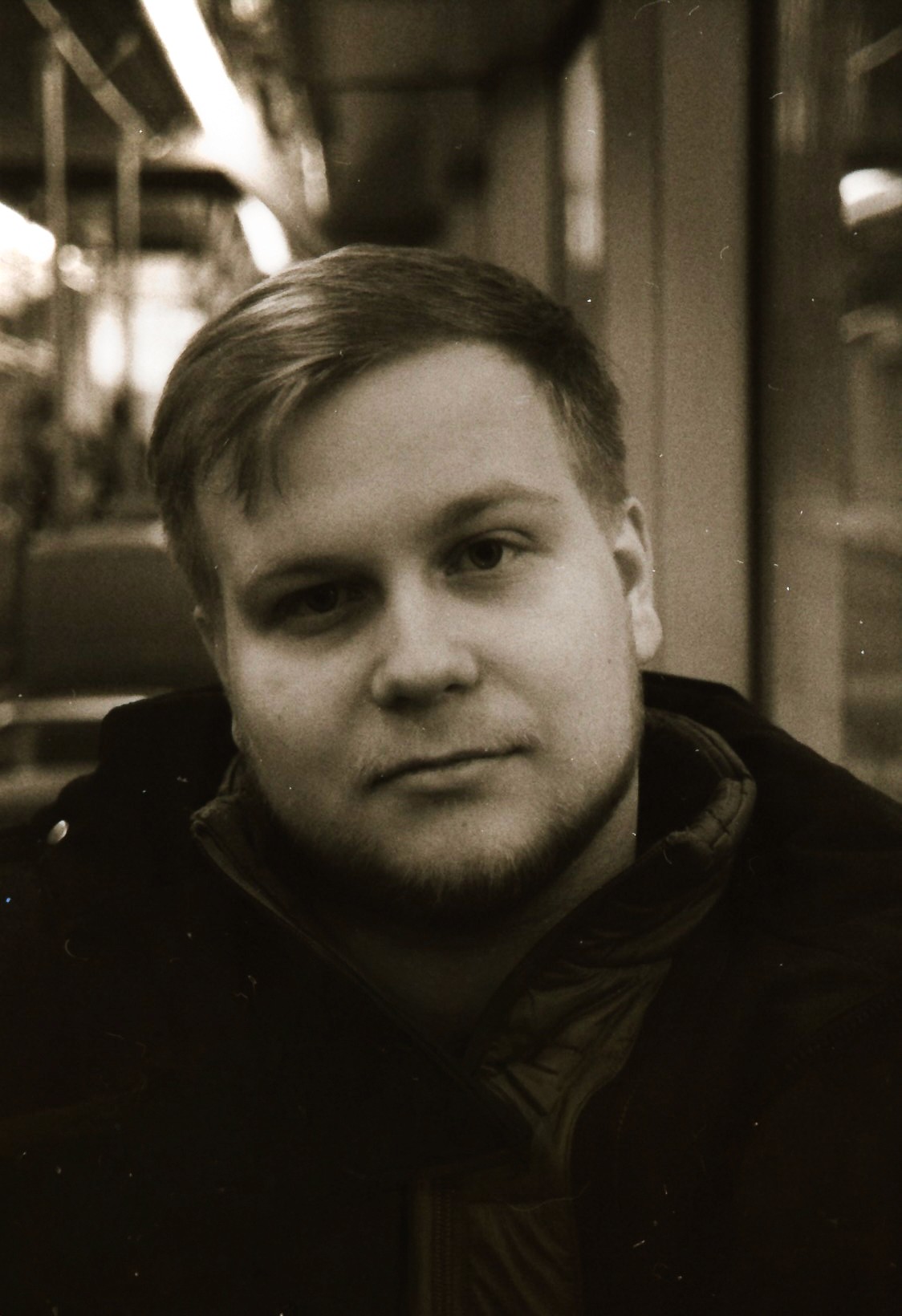 A thoughtful young person with dark hair gazes to the side, captured in soft black and white lighting.