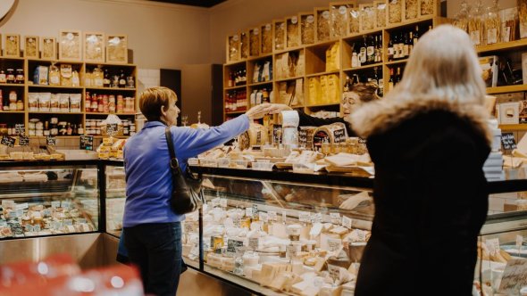 Une cliente échange avec un vendeur devant un comptoir à fromages abondamment garni dans une boutique spécialisée, illustrant l'expérience client personnalisée et le charme du commerce de proximité en Suisse Romande grâce à Marketloca.ch