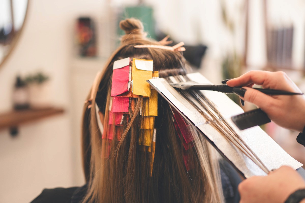 Back view of a client receiving a multi-tone foil highlight service, with pink and yellow foils applied for custom color placement in the salon.
