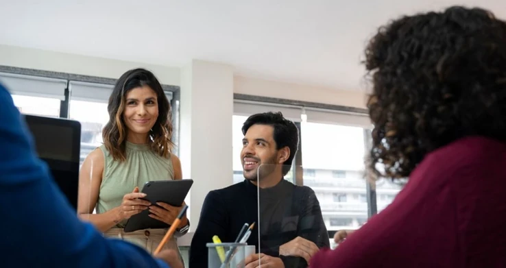 Grupo conversando num escritório claro, um homem segurando um tablet, visto por cima do ombro de uma colega