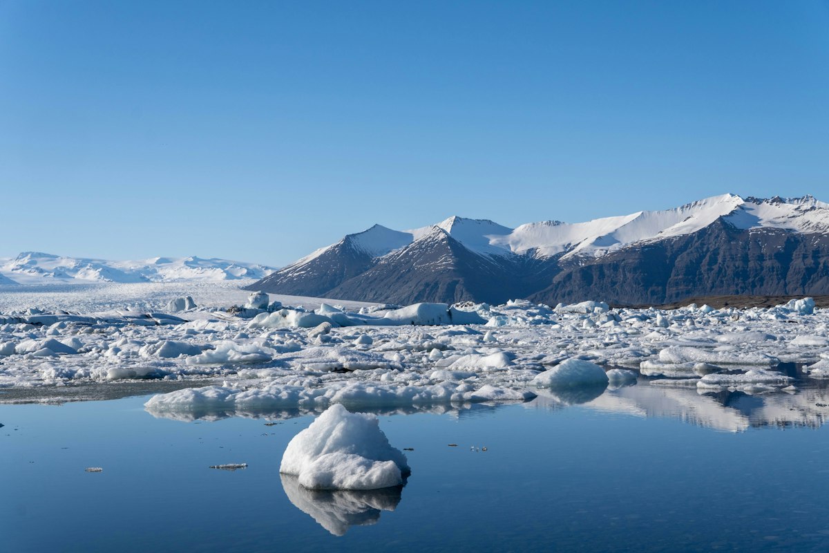 Small icebergs floating in calm blue water at Jökulsárlón glacier lagoon, Iceland, below snow-capped mountains